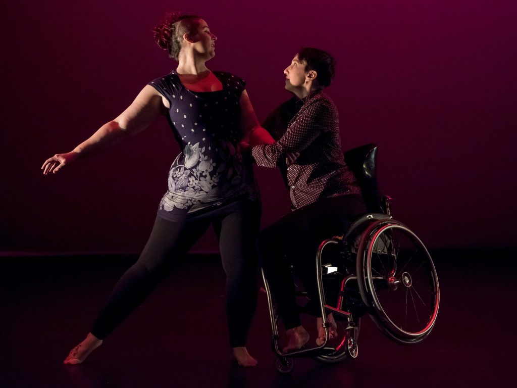 Masculine presenting wheelchair user dances with femme presenting ambulatory dancer. 
 
